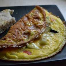 Przepis na Omlet z cukinią, czerwoną papryką i wędzonym łososiem; pół opieczonej bułki ziarnistej.